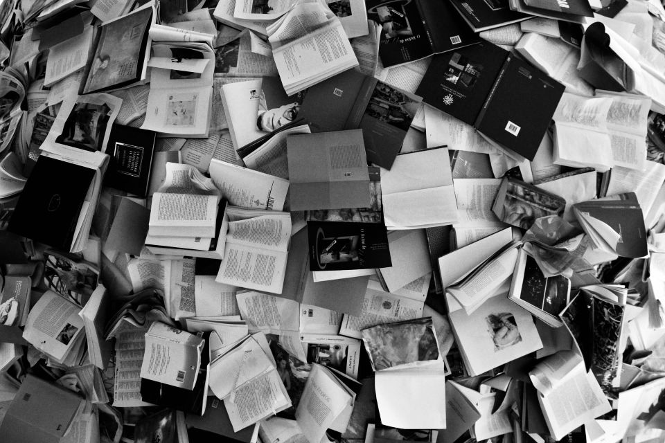 A view from above of various open books, scattered on the floor in an disorderly manner. This image illustrates the challenges of the process of writing a non-fiction book proposal.