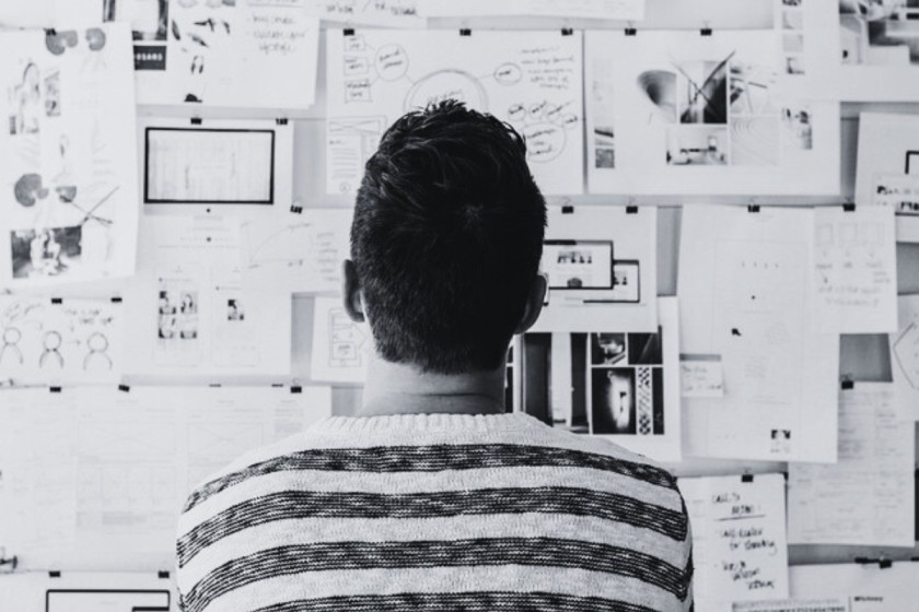 A person in a stripy top facing a wall covered in documents with text and charts. This image illustrates the need to use academic writing tools when creating academic texts.