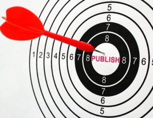 A red dart in the middle of a round black and white dartboard, where the top score in the middle was replaced with the word "publish." this image illustrates the pros and cons of self-publishing, indie and traditional publishing.