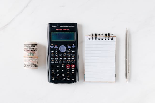 Composition of calculator with paper money and notebook with pen
